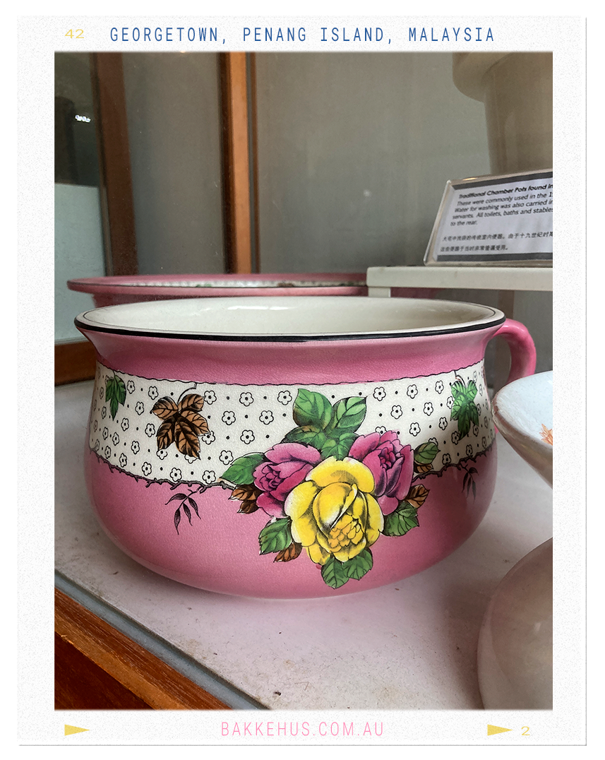 Vintage hand-painted ceramic chamber pot featuring floral motifs in pink, yellow, and green, displayed as part of the Blue Mansion’s historical exhibit in George Town, Penang, Malaysia. A whimsical detail from the mansion’s curated collection. © Heidi Isaksen-Loxton for bakkehus.com