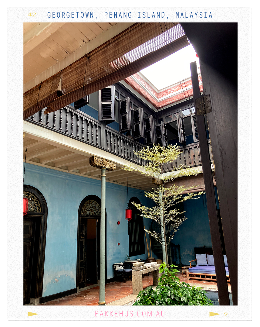 Interior courtyard of the Blue Mansion in George Town, Penang, Malaysia, showcasing blue lime-washed walls, traditional timber shutters, Chinese-style columns, and a central garden beneath an open skylight—highlighting the mansion’s Straits Eclectic architecture. © Heidi Isaksen-Loxton for bakkehus.com