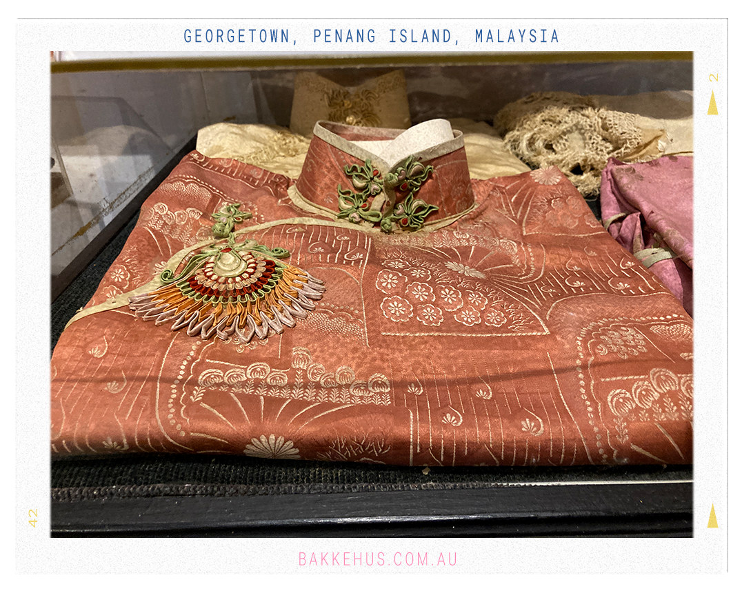 Traditional Chinese garment in rich rust-orange silk with intricate embroidered patterns, part of the Blue Mansion’s historical clothing collection in George Town, Penang, Malaysia. © Heidi Isaksen-Loxton for bakkehus.com
