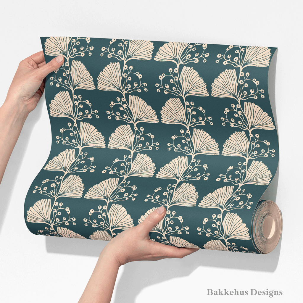 Two hands unroll a length of Art Nouveau Ginkgo Sprig wallpaper, showing the vertical stripes of cream ginkgo leaves and berry sprigs on a deep teal ground.