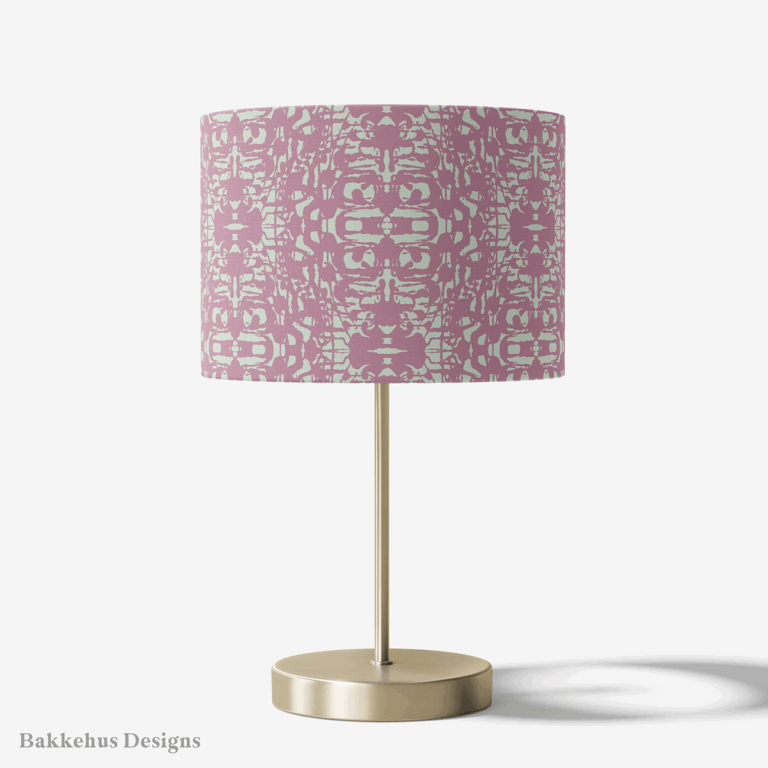 Table lamp with a brass stand and a round drum shade covered in the Abstract Inked Lace pattern in pale sage green and dusty mauve.