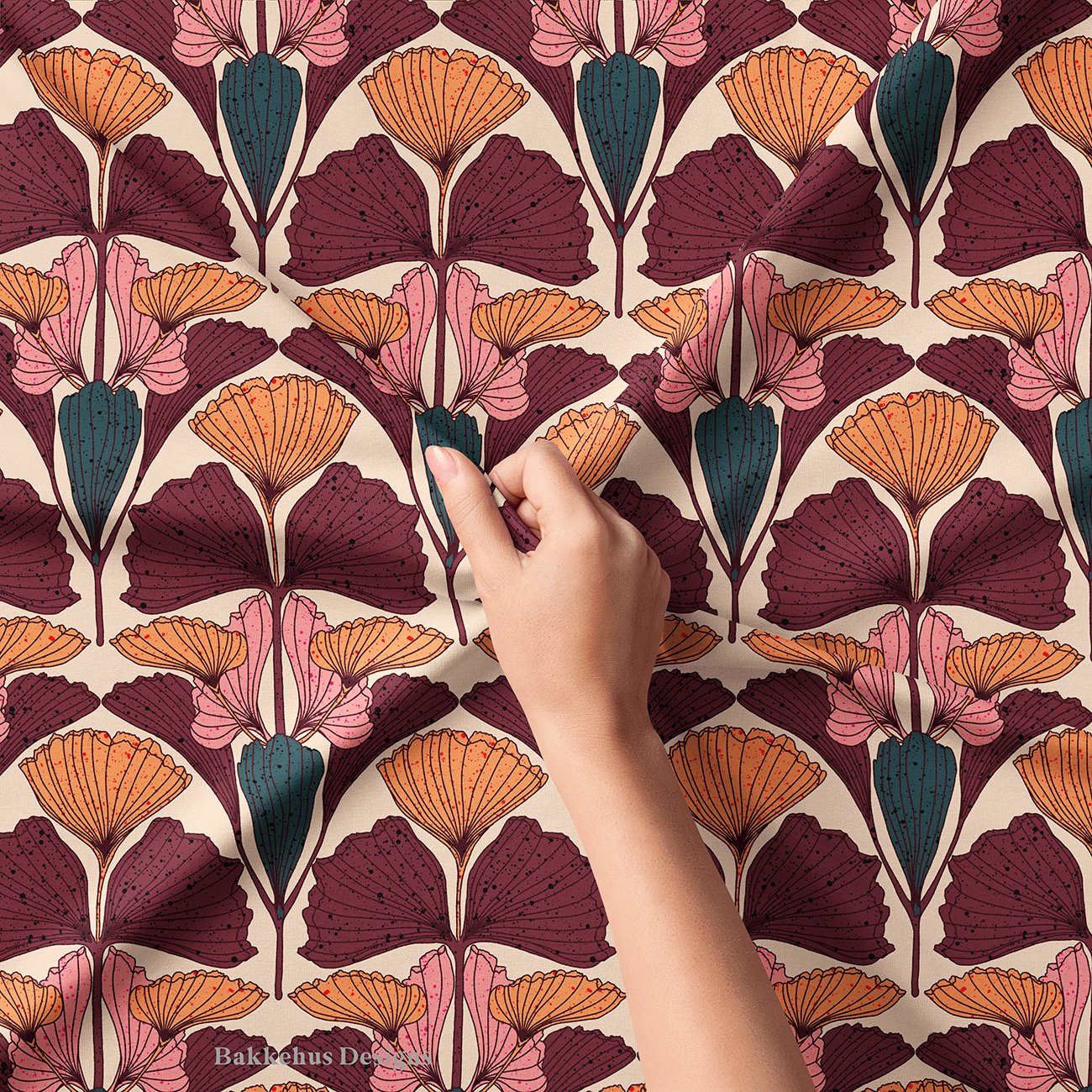 Close-up of a hand lifting Art Nouveau Ginkgo Fan fabric, showing the fine ink lines and speckles on the plum, burnt orange and pink ginkgo fans.