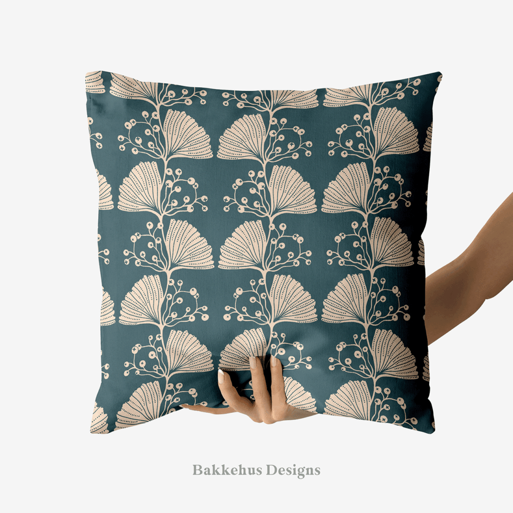 A hand holds up a square cushion printed with Art Nouveau Ginkgo Sprig, a two-colour pattern of stylised cream ginkgo leaves and berry sprigs in vertical stripes on deep teal.