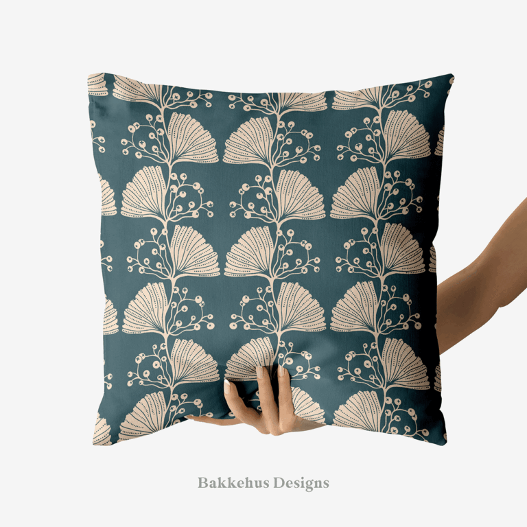 A hand holds up a square cushion printed with Art Nouveau Ginkgo Sprig, a two-colour pattern of stylised cream ginkgo leaves and berry sprigs in vertical stripes on deep teal.