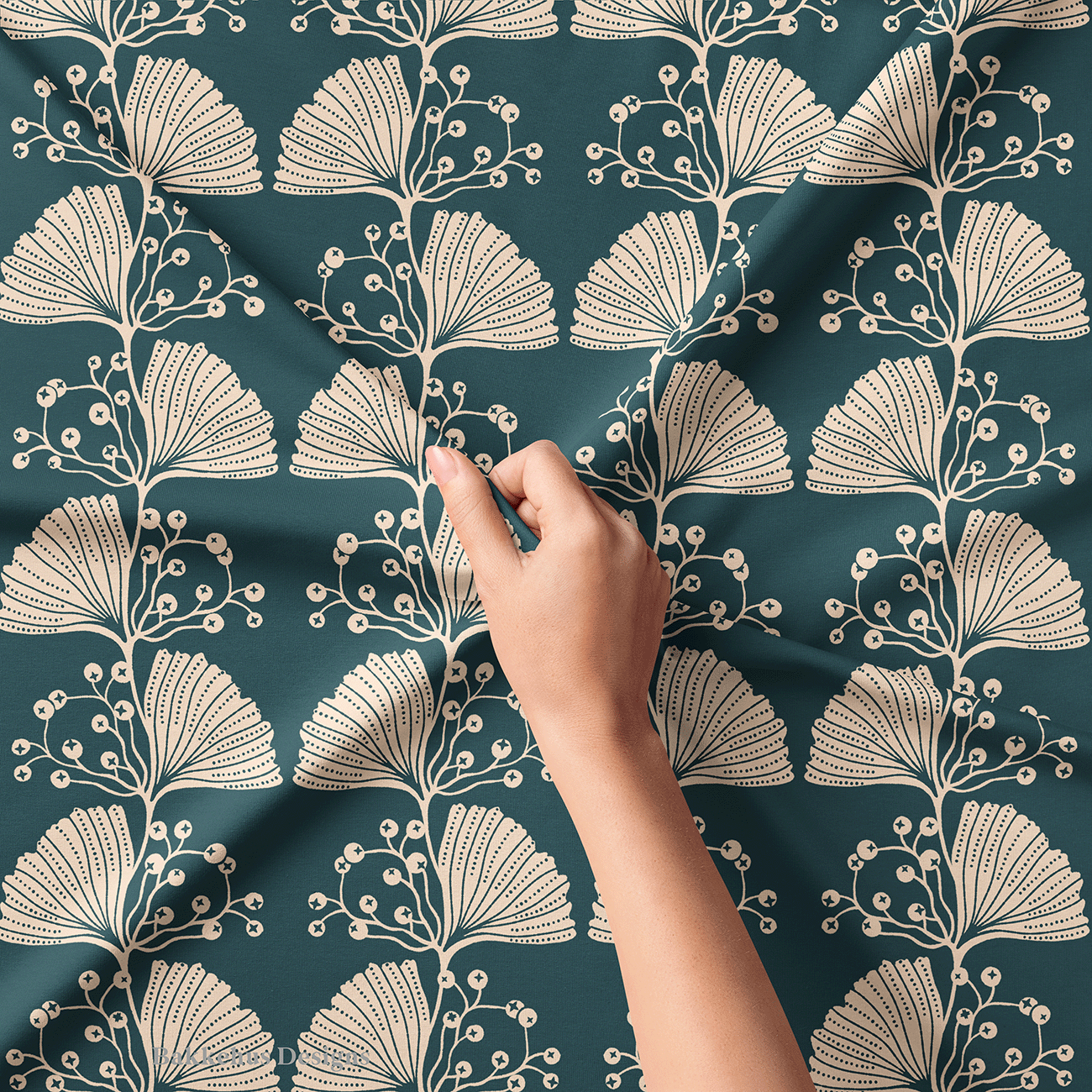 Close-up of a hand lifting Art Nouveau Ginkgo Sprig fabric, showing the fine line work and dotted cut-outs on the cream ginkgo leaves and berry sprigs against deep teal.