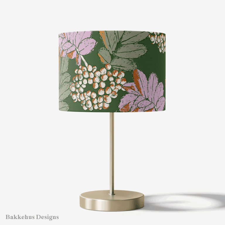 Table lamp with a brass stand and a round drum shade covered in the Bramble & Berry Botanical pattern, with lilac and cream berries and leaves on forest green.