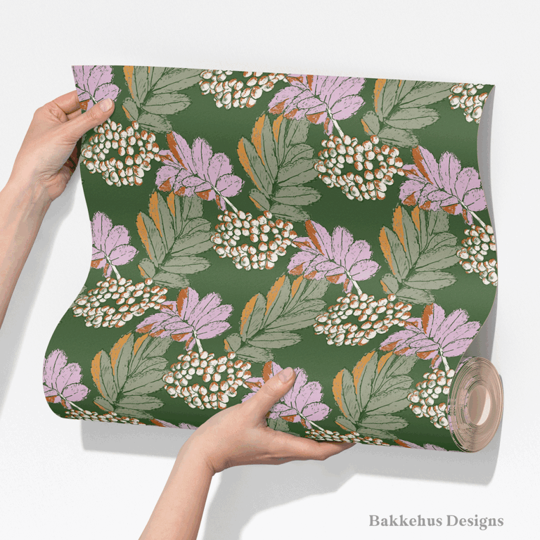 Two hands unroll a length of Bramble & Berry Botanical wallpaper, showing large berry clusters and leafy branches in lilac and cream on forest green.