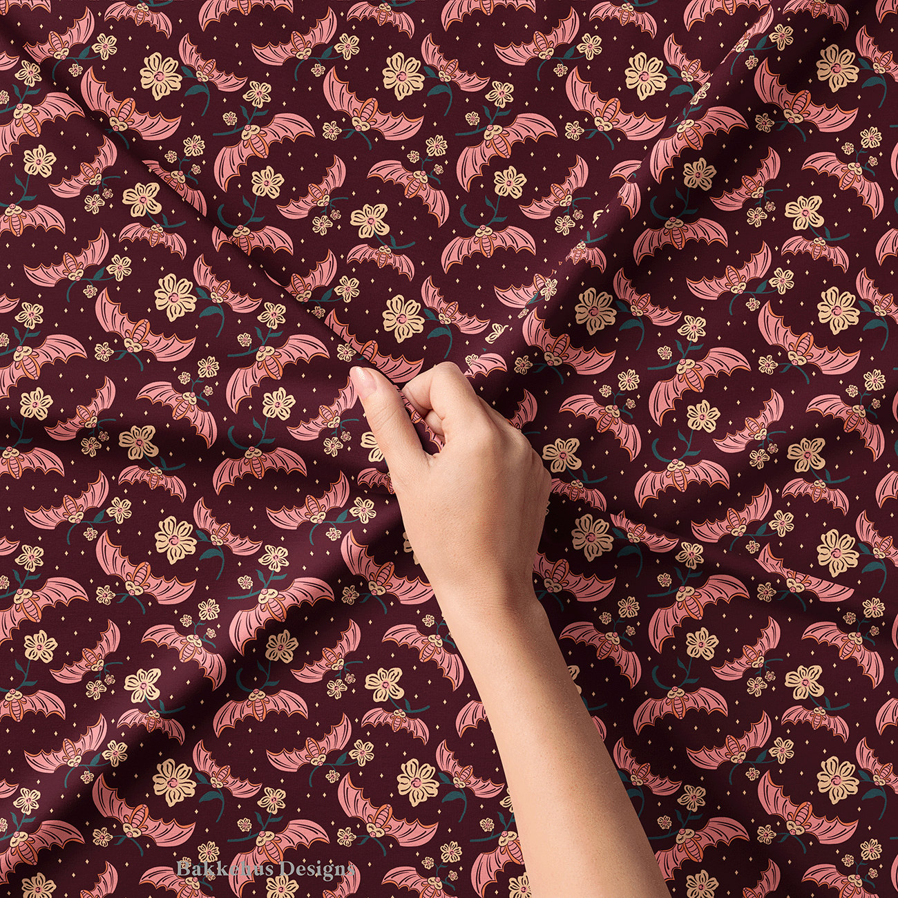 Close-up of a hand lifting Cute Flower Bats fabric, showing the pink bats, cream flowers and tiny sparkles on dark plum.