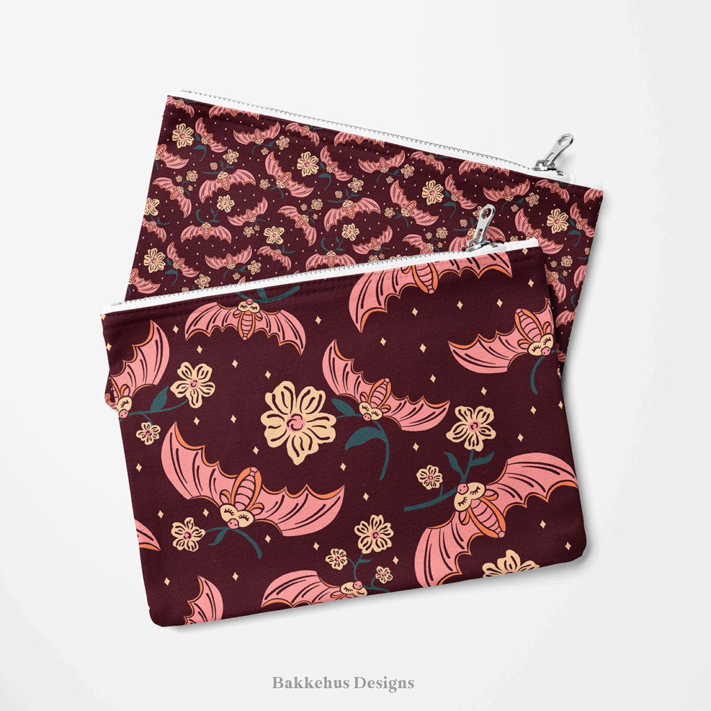 Two zip pouches made from Cute Flower Bats fabric, one lying on the other, printed with pink bats and cream flowers on dark plum.