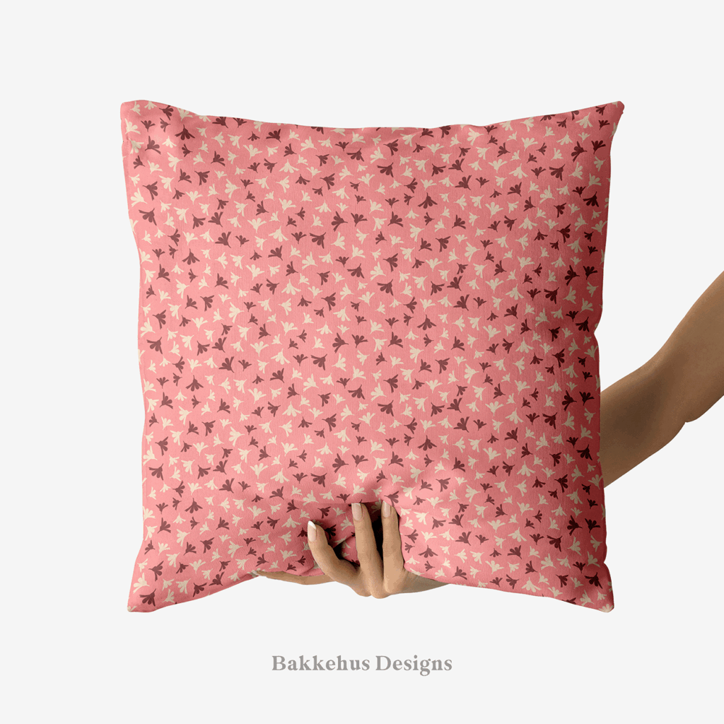 A hand holds up a square cushion printed with Ditsy Flower Sprigs, tiny rosewood and cream flower sprigs scattered over soft pink.