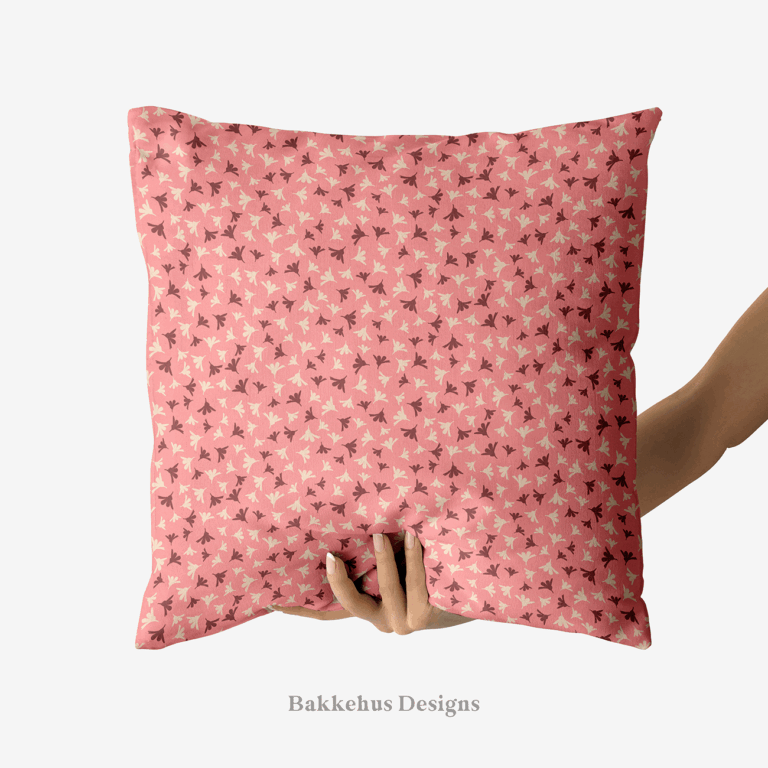 A hand holds up a square cushion printed with Ditsy Flower Sprigs, tiny rosewood and cream flower sprigs scattered over soft pink.