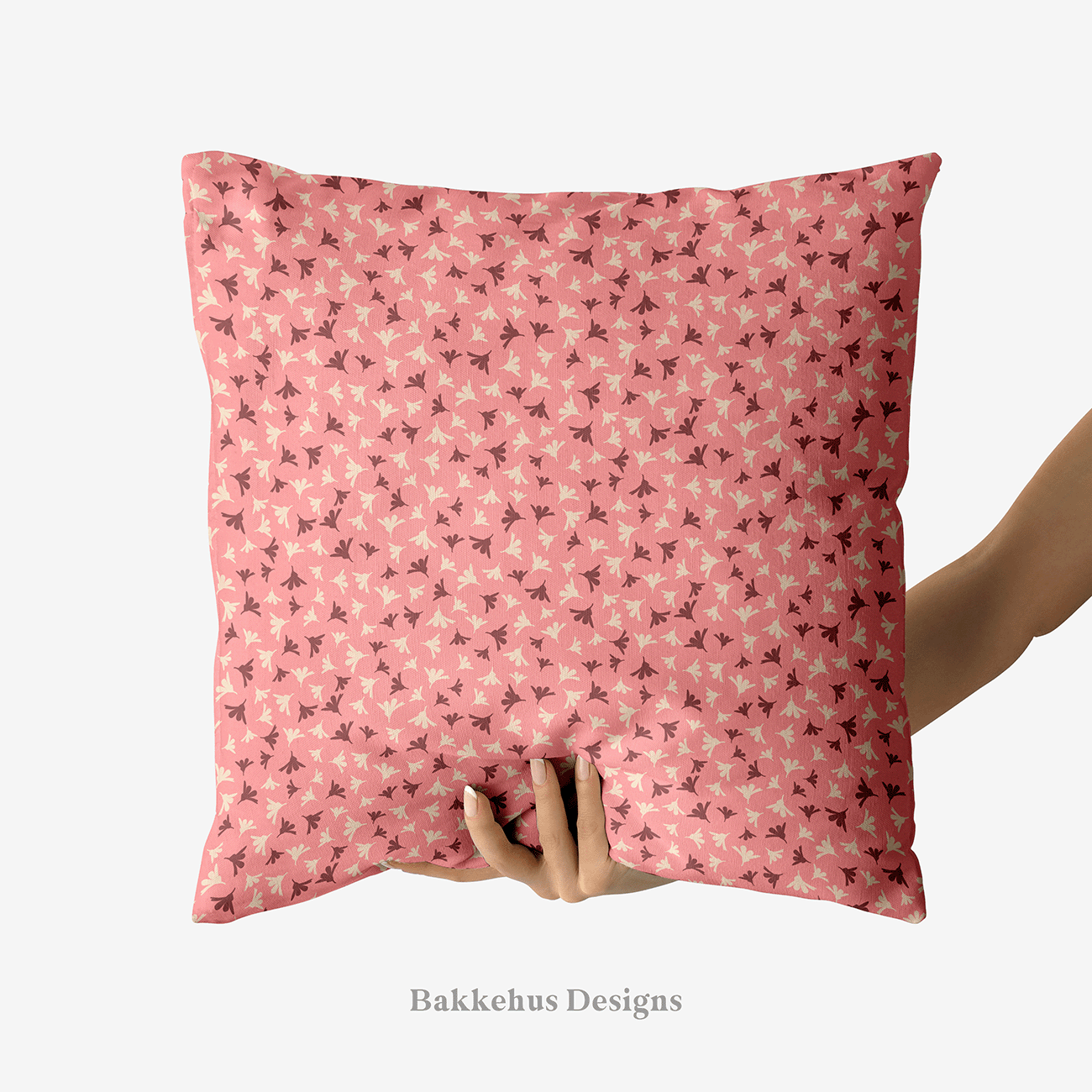 A hand holds up a square cushion printed with Ditsy Flower Sprigs, tiny rosewood and cream flower sprigs scattered over soft pink.