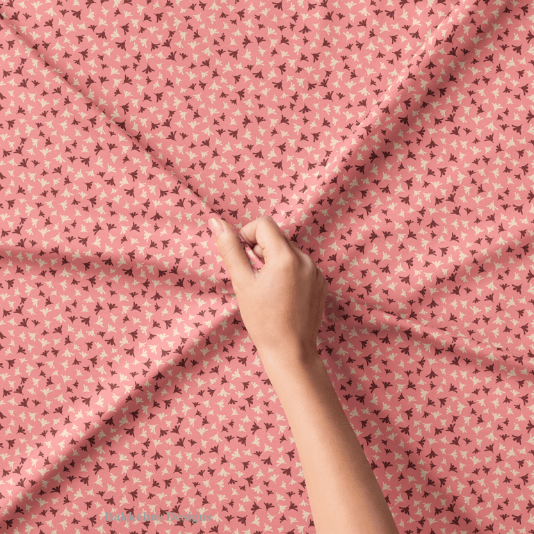 Close-up of a hand lifting Ditsy Flower Sprigs fabric, showing the tiny rosewood and cream sprigs on soft pink.