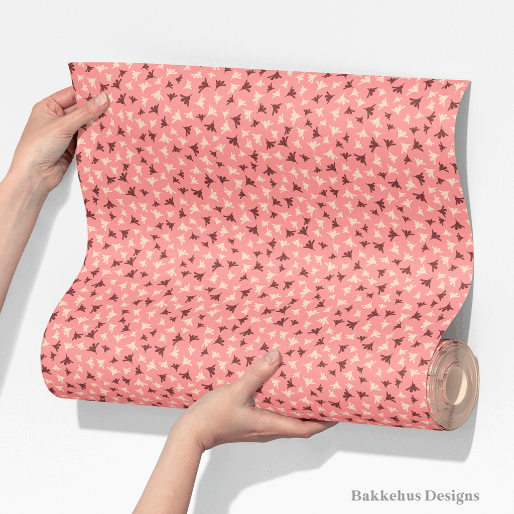 Two hands unroll a length of Ditsy Flower Sprigs wallpaper, showing tiny rosewood and cream flower sprigs scattered over soft pink.