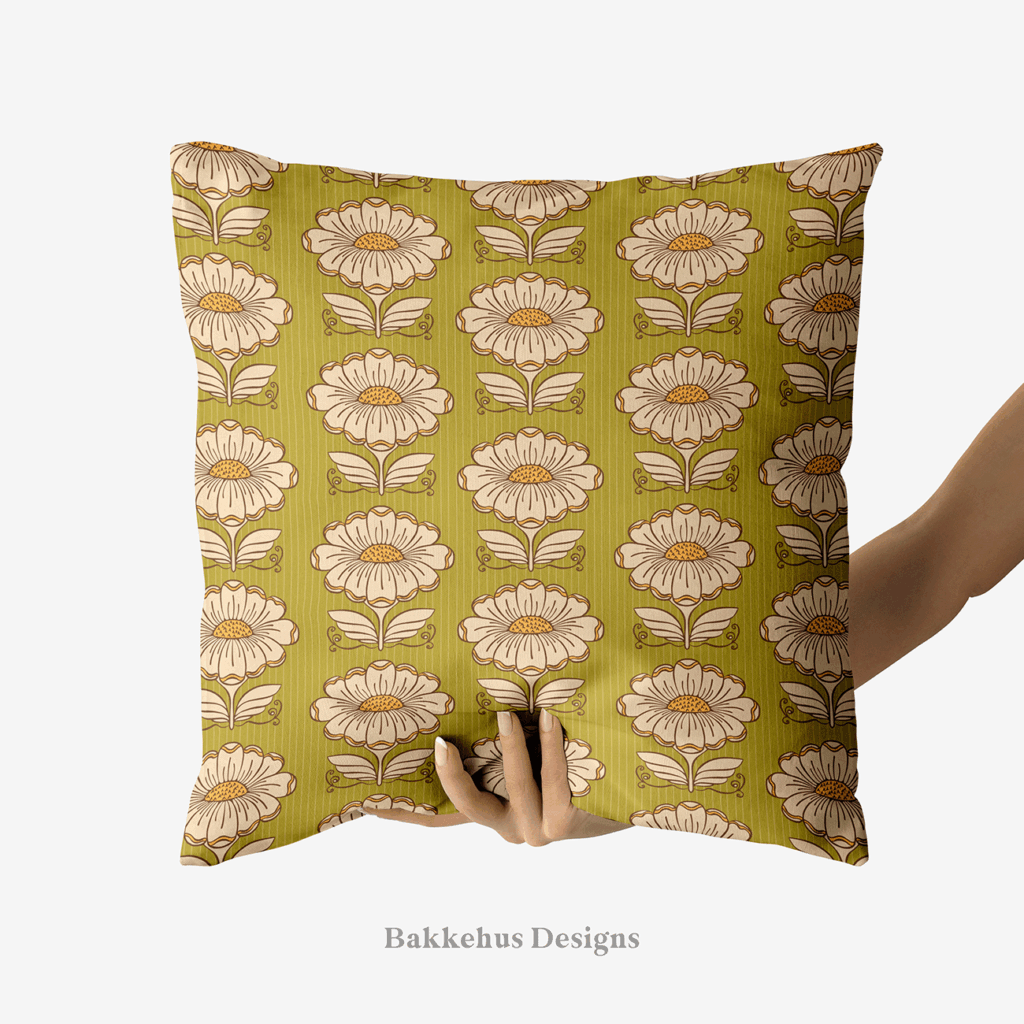 A hand holds up a square cushion printed with Hillside Bloom, a 1970s-style pattern of cream daisies with mustard centres and stylised leaves in rows on olive green.