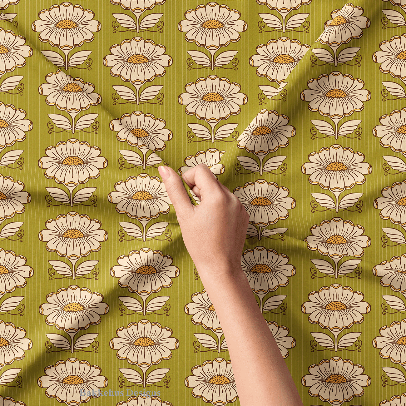 Close-up of a hand lifting Hillside Bloom fabric, showing the cream daisies, dotted mustard centres, brown outlines and the fine pinstripe on the olive green background.