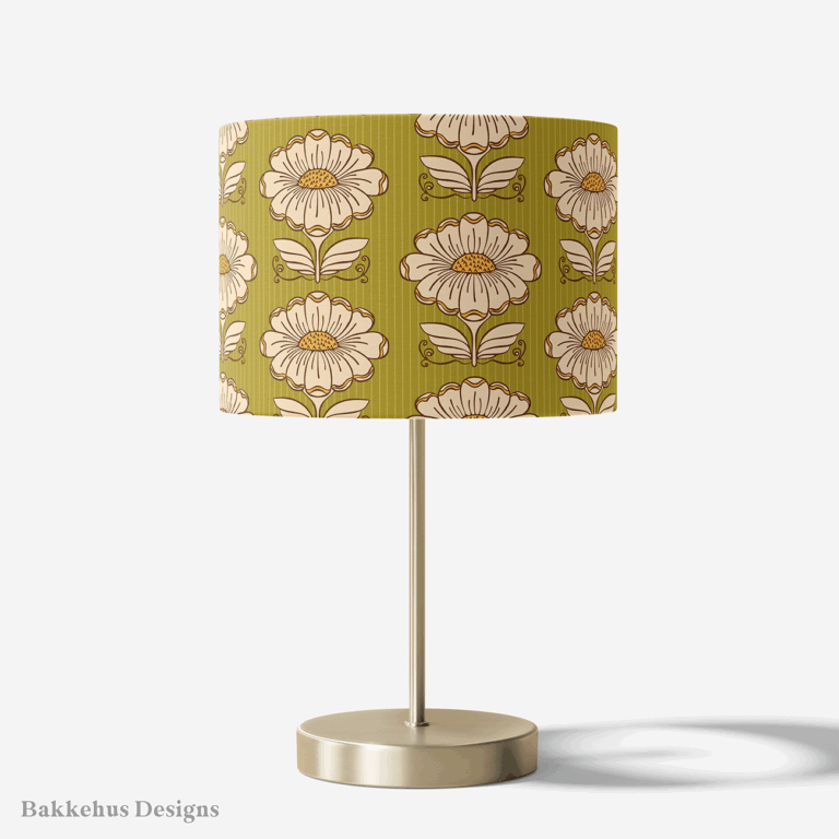 Table lamp with a brass stand and a round drum shade covered in the Hillside Bloom retro daisy pattern, with cream flowers on olive green.