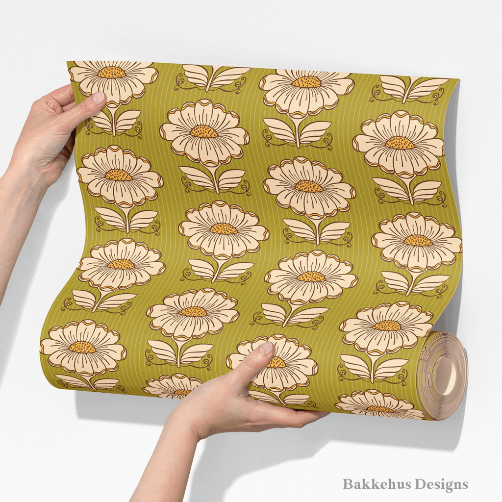 Two hands unroll a length of Hillside Bloom wallpaper, showing rows of cream retro daisies with mustard centres on an olive green background.