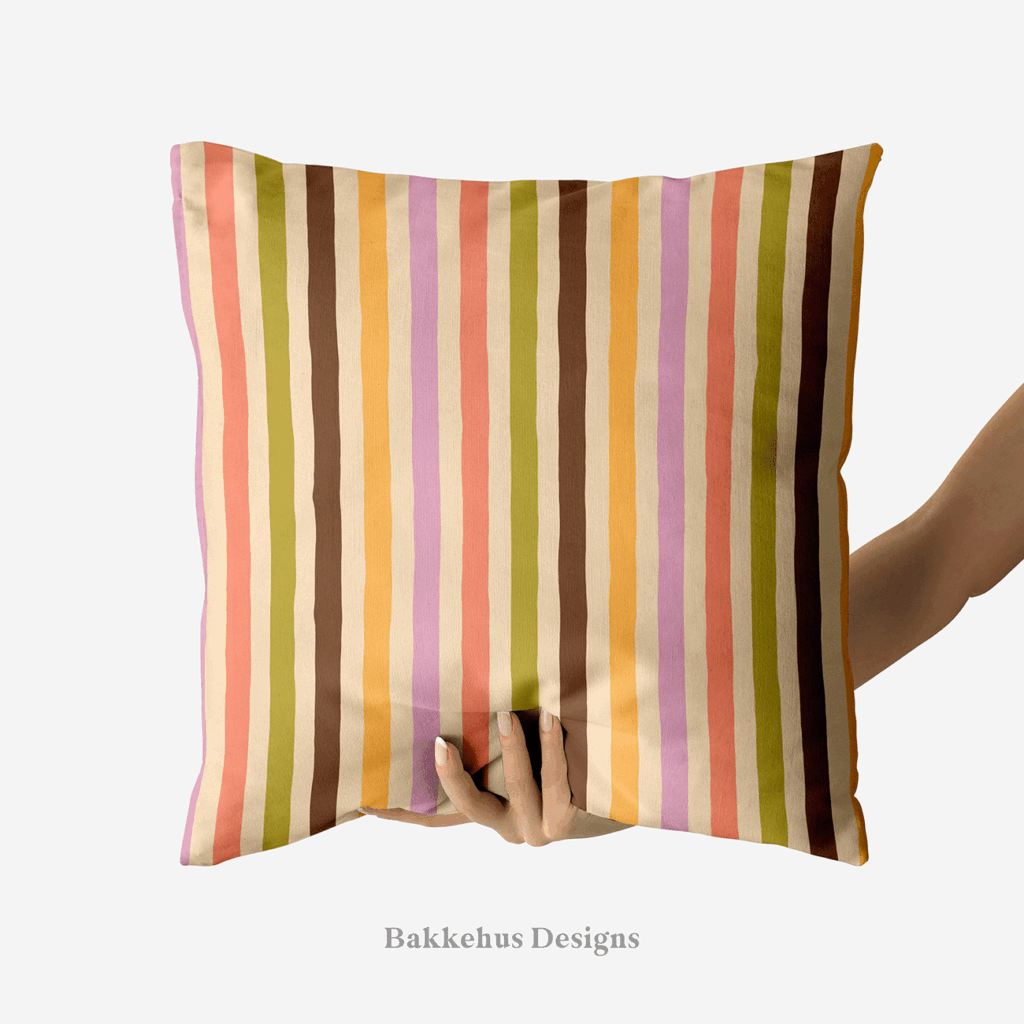 A hand holds up a square cushion printed with Organic Narrow Stripe, a hand drawn vertical stripe in earthy retro colours on cream.