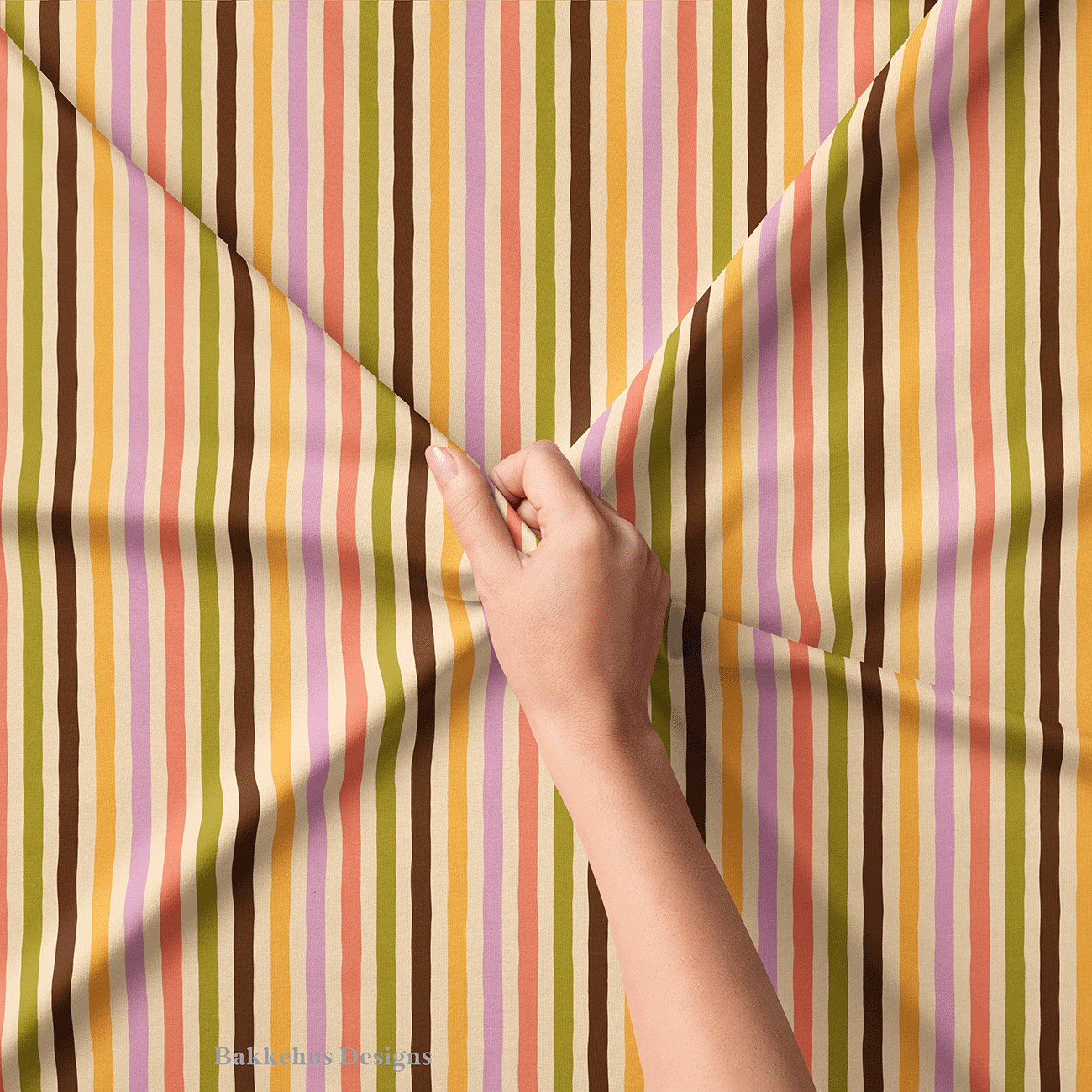 Close-up of a hand lifting Organic Narrow Stripe fabric, showing the uneven hand drawn edges of the narrow stripes in earthy retro colours.