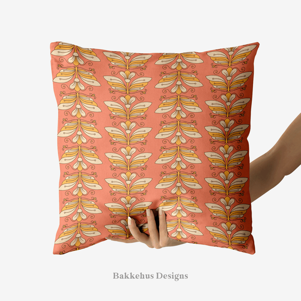 A hand holds up a square cushion printed with Retro Flower Moth Stripe, an Art Nouveau-inspired pattern of stylised cream and gold flower moths in vertical stripes on a coral ground.