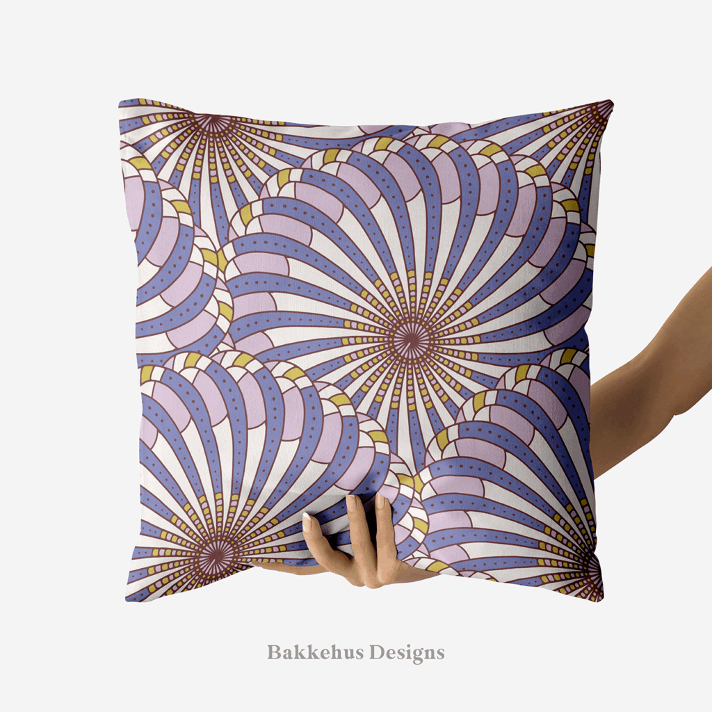 A hand holds up a square cushion printed with Retro Gatsby Disco, a large-scale Art Deco scallop fan pattern in cornflower blue and lilac. Overlapping fans radiate from dark centres, with dotted bands on a cream ground.