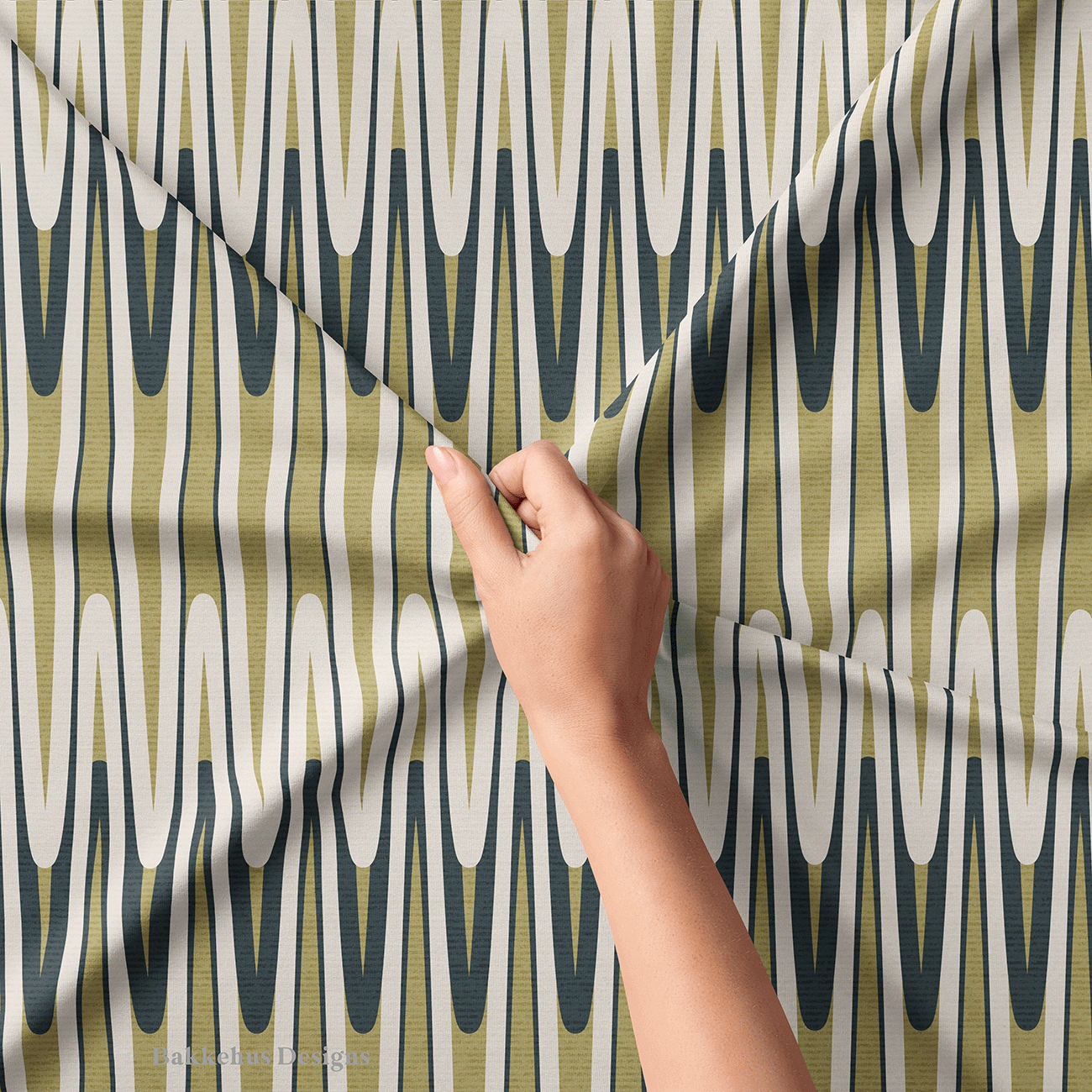 Close-up of a hand lifting Retro Wavy Stripe fabric, showing the olive green and charcoal looping waves and thin vertical lines that create a subtle optical effect.