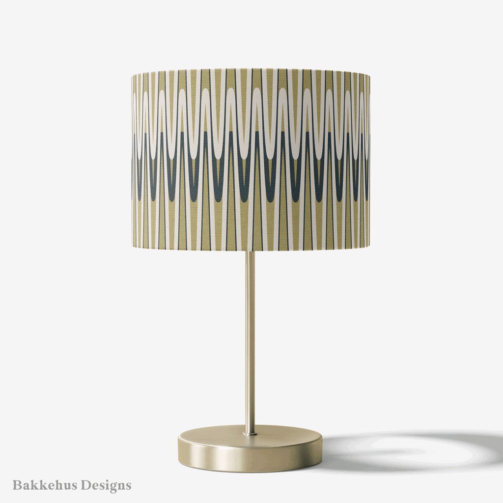 Table lamp with a brass stand and a round drum shade covered in the Retro Wavy Stripe pattern, with olive green and charcoal waves on cream.