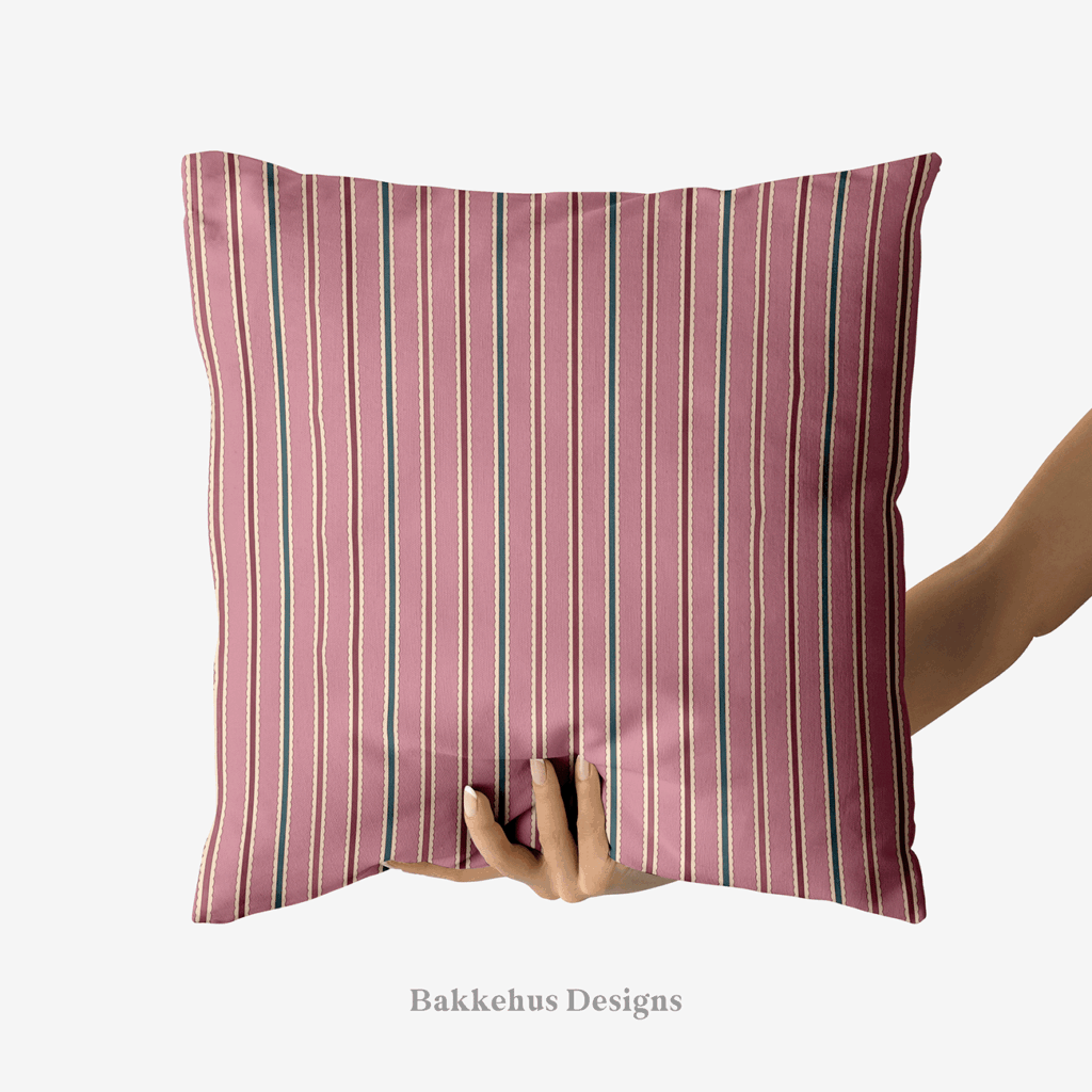 A hand holds up a square cushion printed with Scalloped Cabana Stripe, a vertical stripe in mauve, deep teal and burgundy edged with a cream scallop.