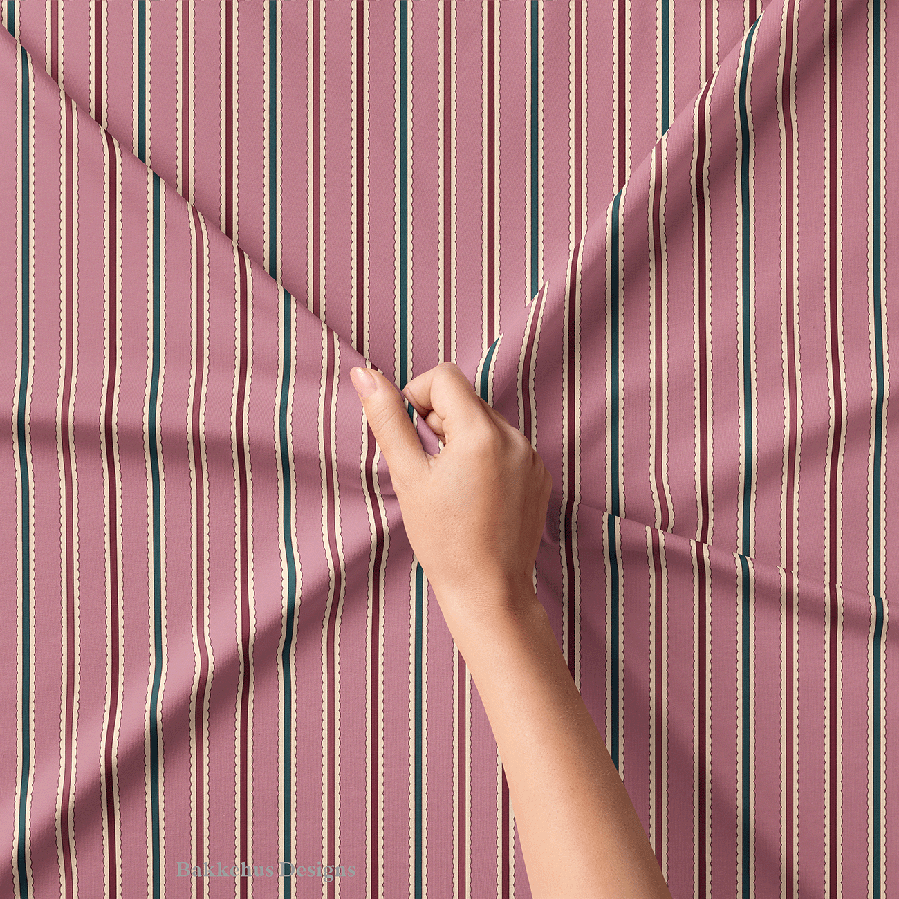 Close-up of a hand lifting Scalloped Cabana Stripe fabric, showing the hand drawn lines and cream scalloped edges between the mauve, deep teal and burgundy stripes.