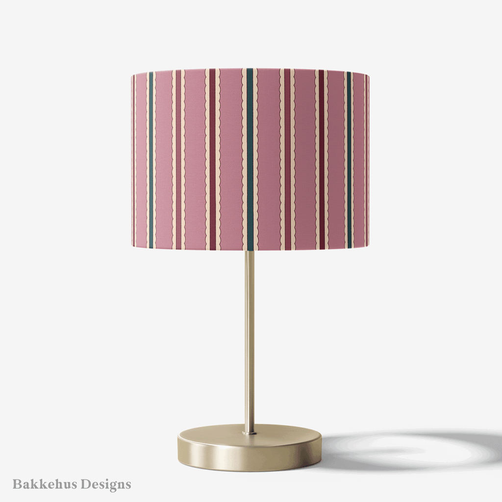 Table lamp with a brass stand and a round drum shade covered in Scalloped Cabana Stripe, a vertical stripe in mauve, deep teal and burgundy.