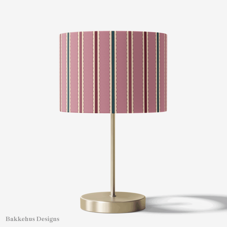 Table lamp with a brass stand and a round drum shade covered in Scalloped Cabana Stripe, a vertical stripe in mauve, deep teal and burgundy.