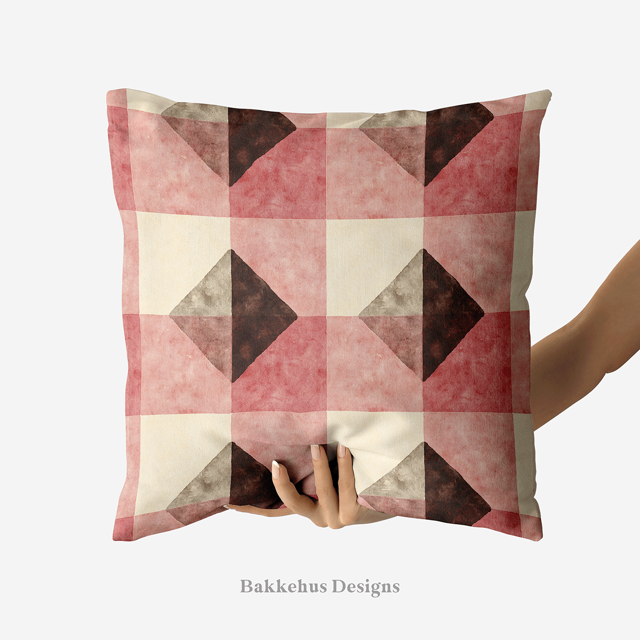 A hand holds up a square cushion printed with Textured Brown Diamond Check, a geometric check of deep brown diamonds and muted clay-rose blocks on a cream background.