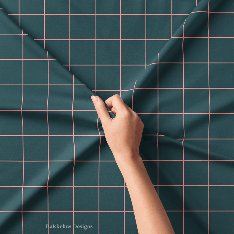 Close-up of a hand lifting Windowpane Check fabric, the pink grid lines on deep teal pulled into soft folds.