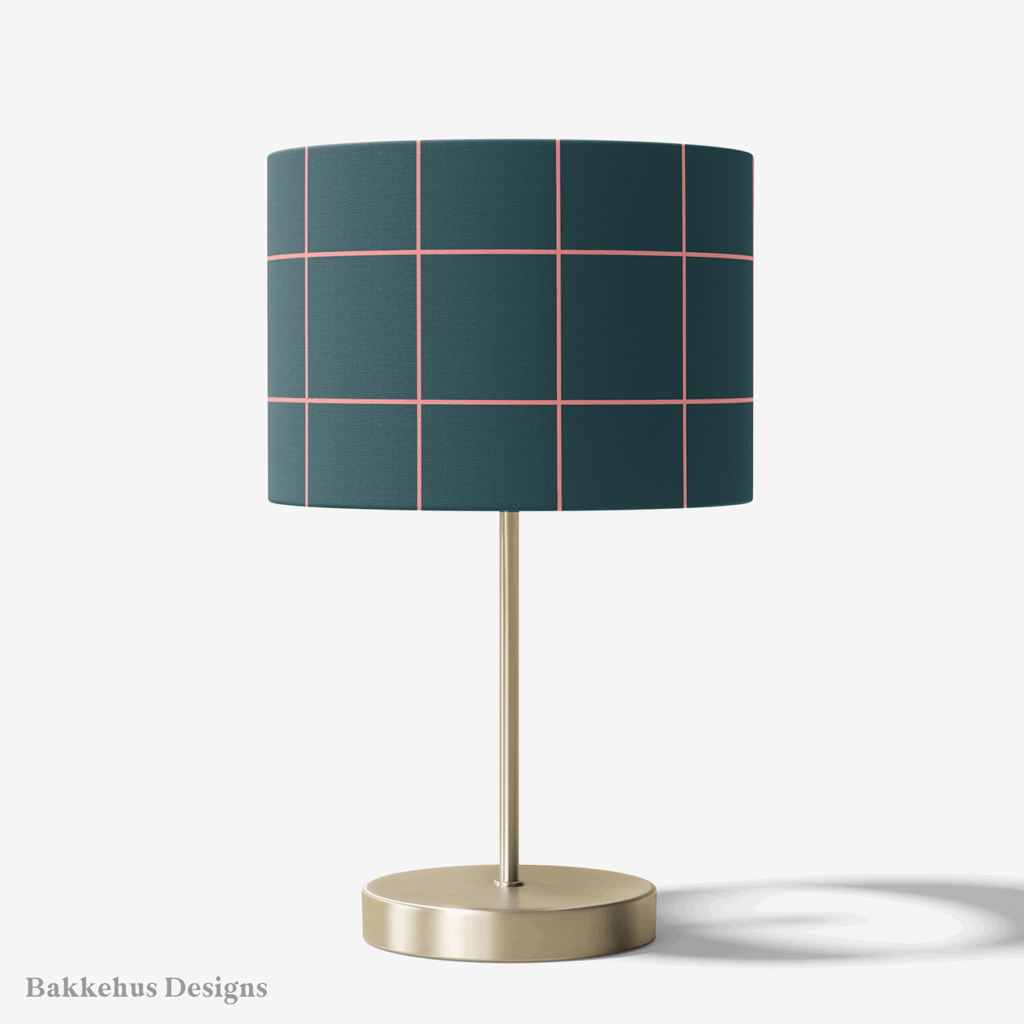 Table lamp with a brass stand and a round drum shade covered in Windowpane Check, a large pink grid on deep teal.